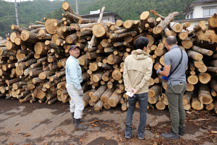 様々な樹種が積み上げられている山の前に立つ堀口さん